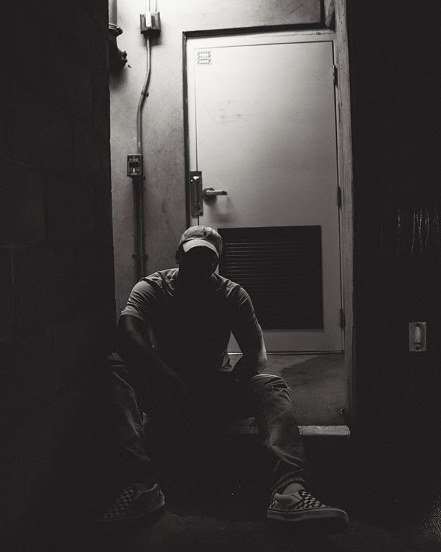 A figure sits in a dark hallway, emphasizing shadows and a monochrome aesthetic.