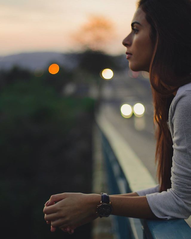 A woman gazes thoughtfully into the distance on a bridge at dusk, evoking peace and tranquility.