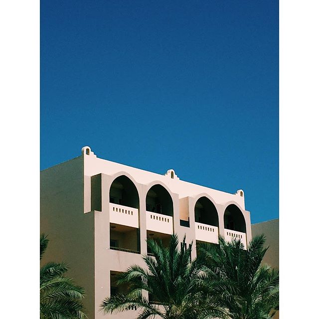 A sunlit building with archways is surrounded by palm trees against a clear blue sky.