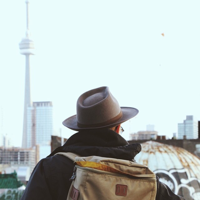 A man with a hat and backpack gazes over a cityscape, creating a sense of urban exploration and calm.