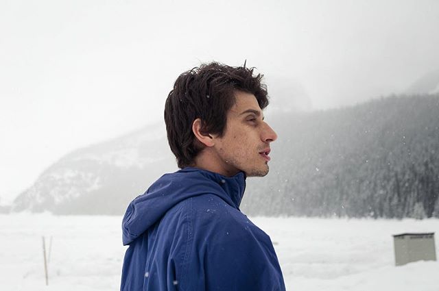 A man in a blue jacket looks out at a snowy mountain landscape during winter.