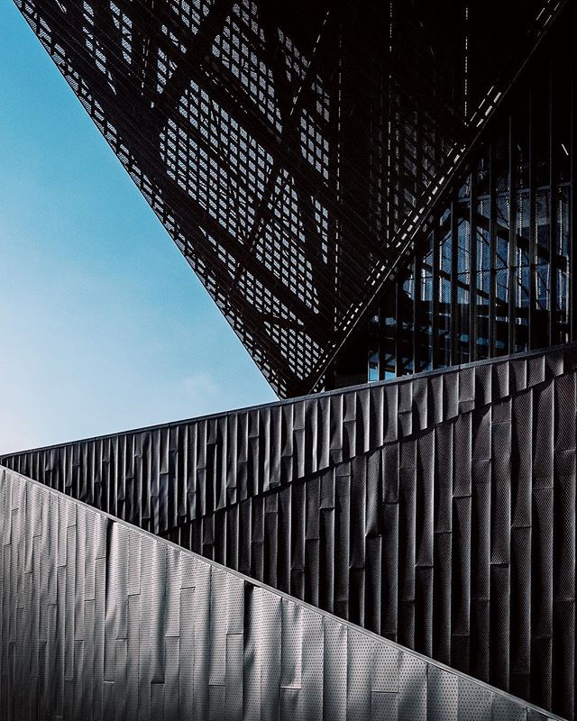 Abstract architectural view of a modern building with geometric lines and a dark facade against a blue sky.