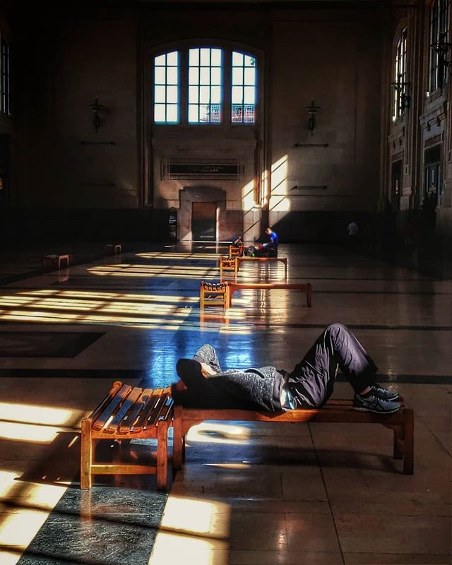 Person lounges on a bench in sun-drenched hall, finding a moment of respite.
