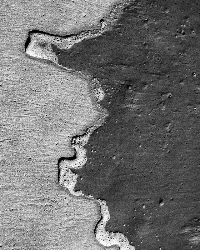 A monochrome close-up shows a wave receding on the sand creating a serene seaside scene.