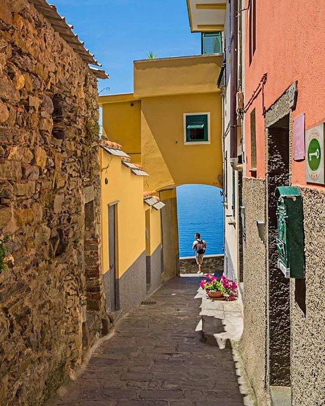 A narrow alley in an Italian coastal town leads to a stunning view of the sea.