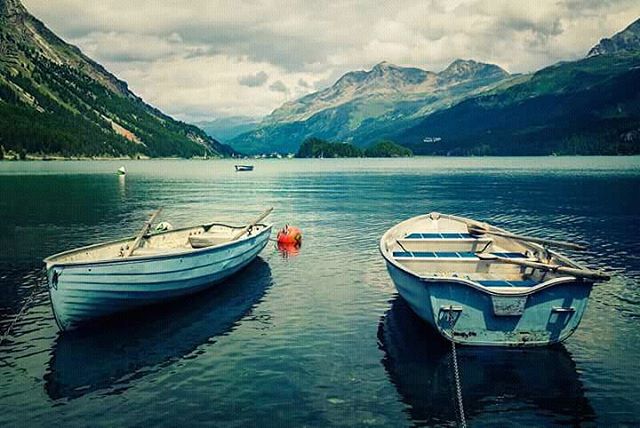 Two rowboats rest on a calm lake surrounded by mountains under a cloudy sky, evoking tranquility.