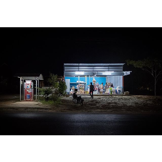 A nighttime scene shows a well-lit shop on the street, with customers and a vintage gas pump.