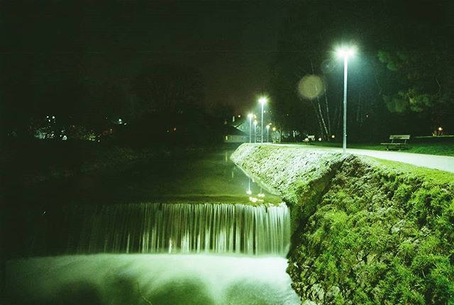 A tranquil waterfall at night in an urban park setting, illuminated by street lights.
