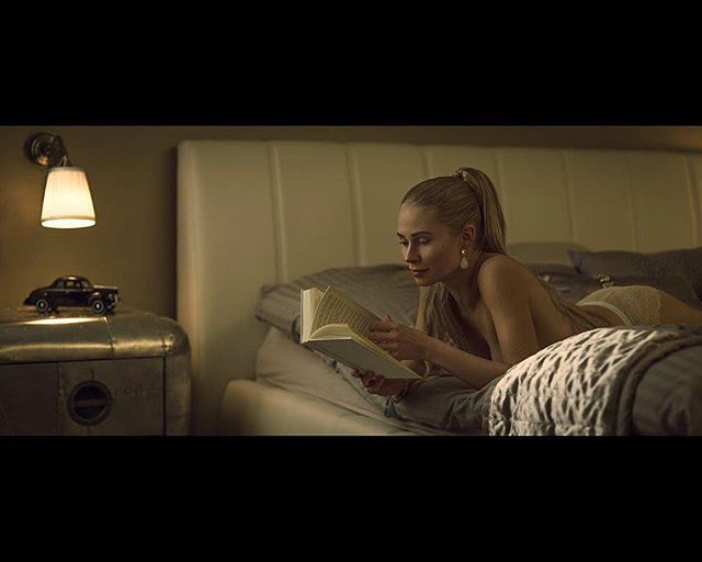 A woman relaxes in bed, reading a book under the soft glow of a bedside lamp.