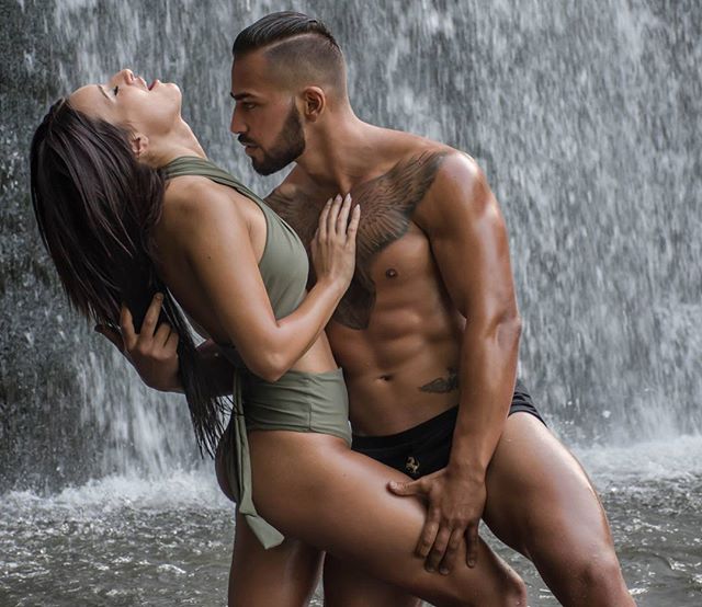 A couple poses intimately by a waterfall, showcasing love and connection in a natural setting.