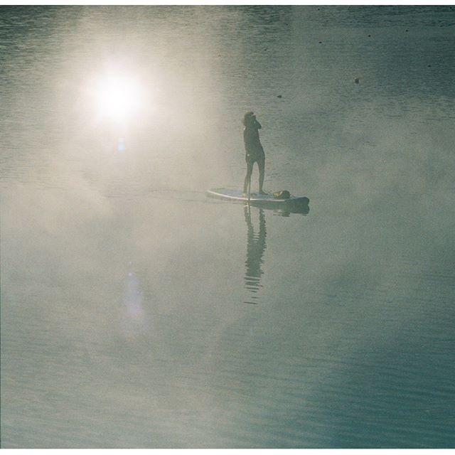 A woman paddleboards on a calm lake under a bright sun, creating a tranquil scene.
