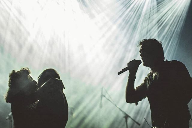 A singer performs on stage in silhouette while a couple embraces in the audience at a concert.