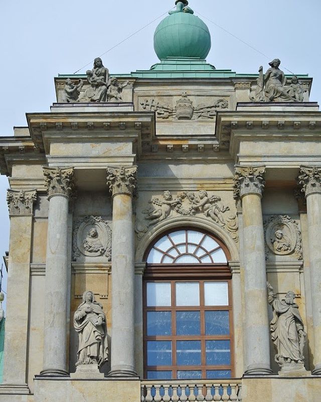 Ornate building facade featuring statues, columns and a green dome, showcasing classical architectural design.
