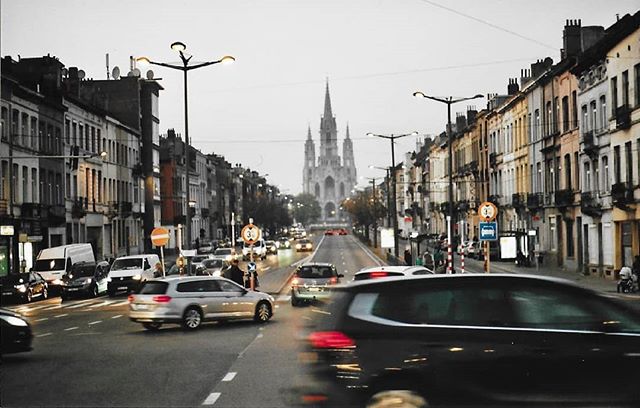 City street scene with traffic and buildings leading to a church in the distance.