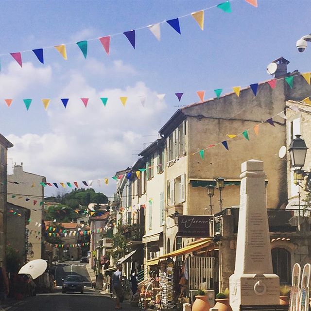 A picturesque street in a charming village, adorned with colorful flags and classic architecture under a sunny sky.