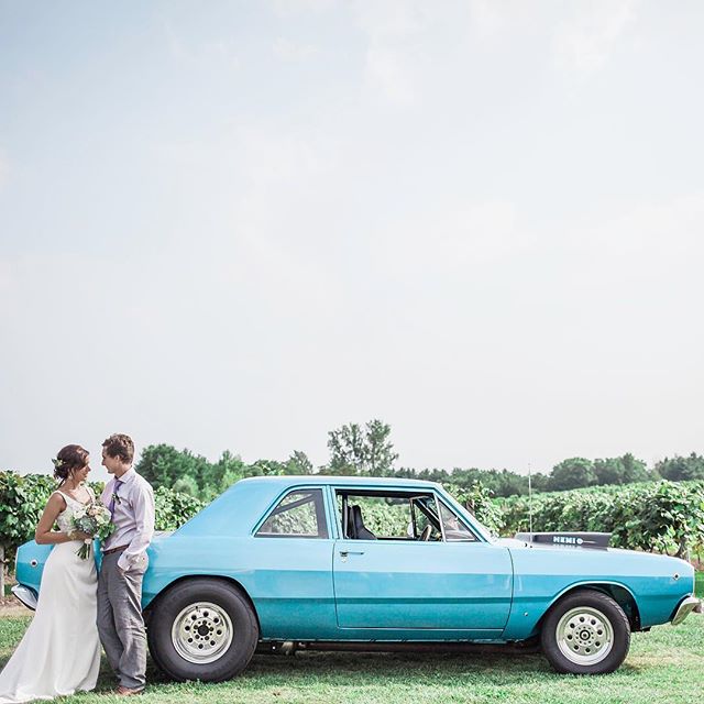 A bride and groom pose by a vintage blue car on their wedding day. The couple enjoys a romantic outdoor celebration.