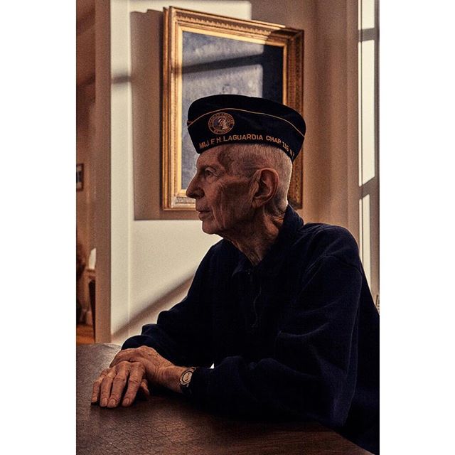 Portrait of a senior man wearing a military hat, sitting at a table in a sunlit room.