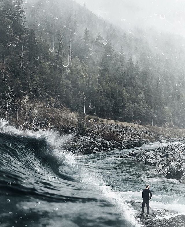 A lone figure stands by a river as a wave approaches, with a forest in the background.