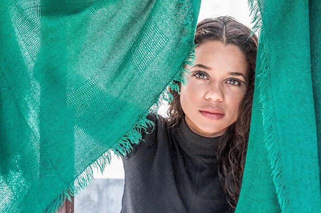 A serene woman peers out from behind a green scarf, creating a peaceful and intimate portrait.