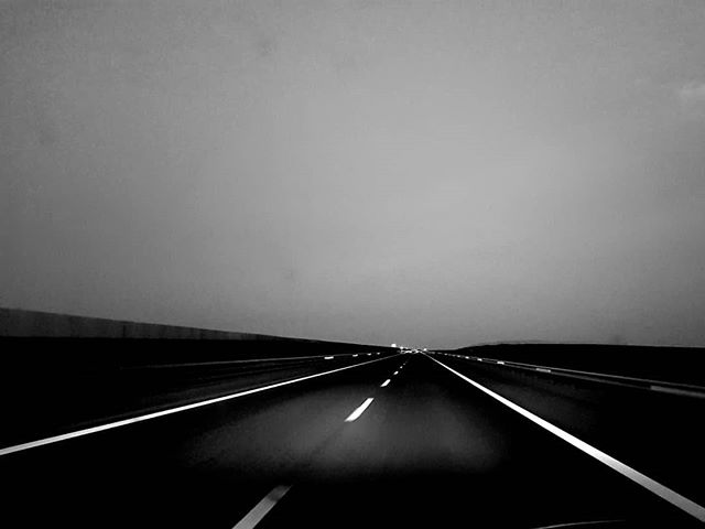 A monochrome view of a straight highway under a cloudy sky, conveying a sense of travel and open road adventures.