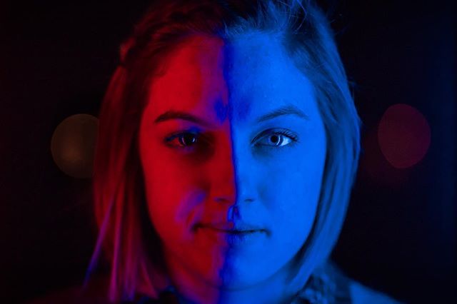 Striking studio portrait of a woman's face split by red and blue lighting creating a dramatic, modern aesthetic.