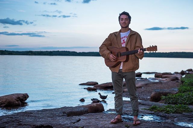 A man plays guitar by a calm lake at dusk, creating a tranquil and inviting outdoor scene.