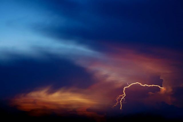 A vivid lightning strike illuminates a dramatic night sky filled with colorful clouds during a powerful storm.