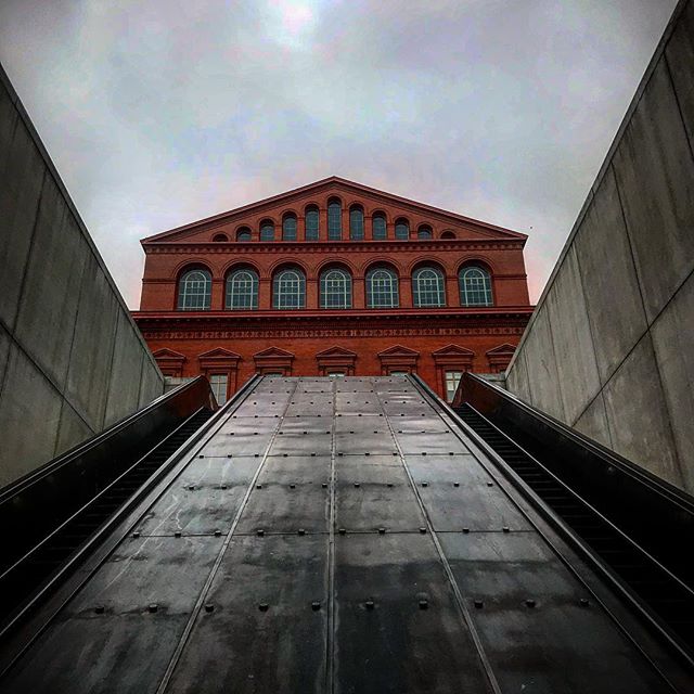 A striking view of a red brick building framed by an escalator, offering an urban and architectural perspective.