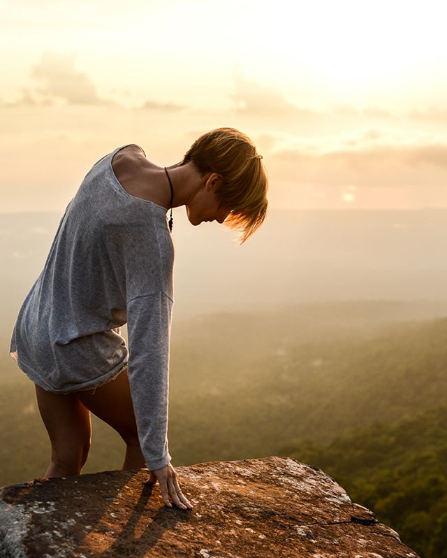 A young woman gazes into the hazy distance from a rocky mountain top at sunset.