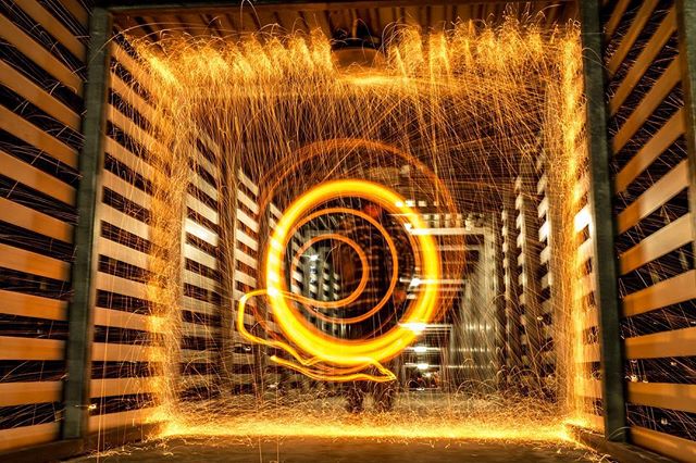 Abstract long exposure of spinning steel wool creating light trails and sparks in an industrial setting, resulting in a vibrant, energetic visual.