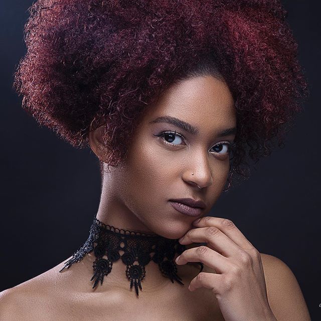 Elegant portrait of a woman with afro hair and a lace choker in a studio setting.