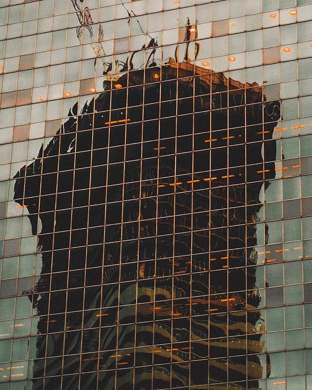 A modern building's glass facade reflects another building, creating an abstract and urban scene.