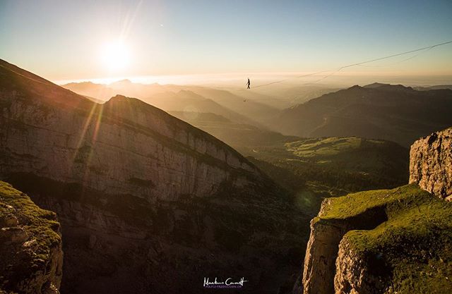 A person balances on a highline strung between mountains at sunrise.