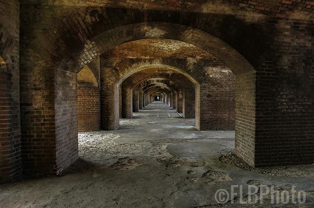 A long, shadowed corridor of brick arches in a historic fort creating an atmospheric perspective.