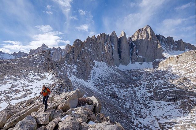 A hiker traverses a rocky, snowy mountain landscape on a sunny day, perfect for adventure and outdoor exploration.