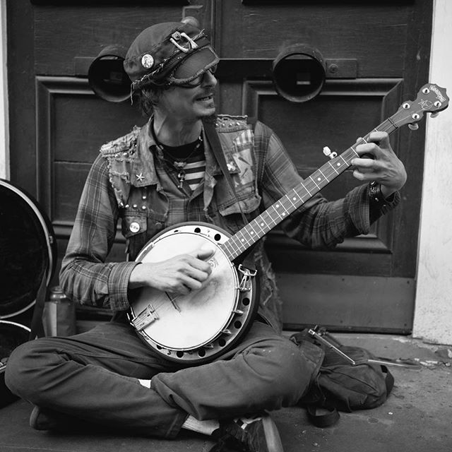 A street musician sits cross-legged and plays the banjo in a black and white shot.