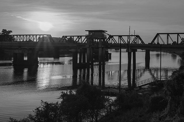 A black and white landscape showcasing a bridge over a calm river during sunset, ideal for themes of travel and architecture.