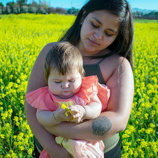 A woman holds a baby in a yellow flower field, creating a touching moment of love and nature.
