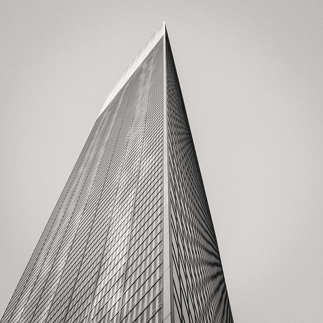 A striking low-angle shot of a modern skyscraper, showcasing its sleek design against a neutral sky.