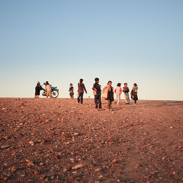 A group of children are seen next to a blue motorcycle on a hilltop landscape.