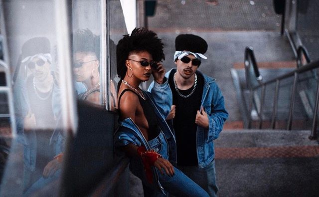 Stylish couple in retro fashion posing outdoors with sunglasses and streetwear for an edgy urban vibe.