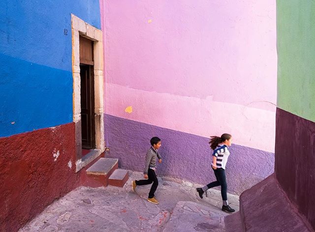 Two children run along a colorful street in a vibrant urban setting with painted walls.