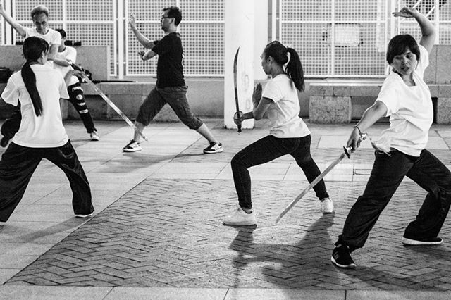 A group of people practices martial arts with swords outdoors in a black and white image.