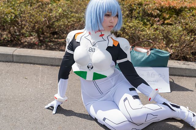A woman in Rei Ayanami cosplay posing in an outdoor setting during the day.