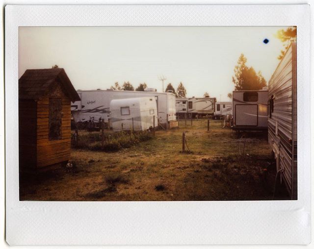 An old-fashioned photo of trailers and a small shed at a campsite with trees in the background.