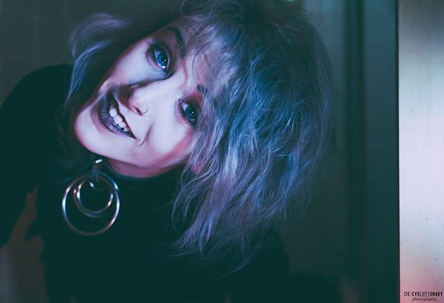 A woman with blue hair and dark lipstick poses in a close-up, moody portrait.