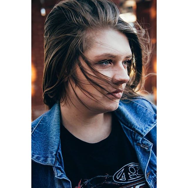 Portrait of a woman with windblown hair wearing a denim jacket, looking off to the side.