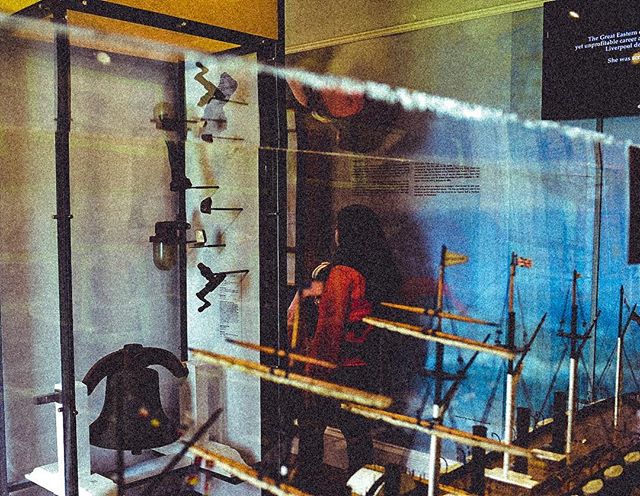 Display case with ship models and a bell in a museum setting.