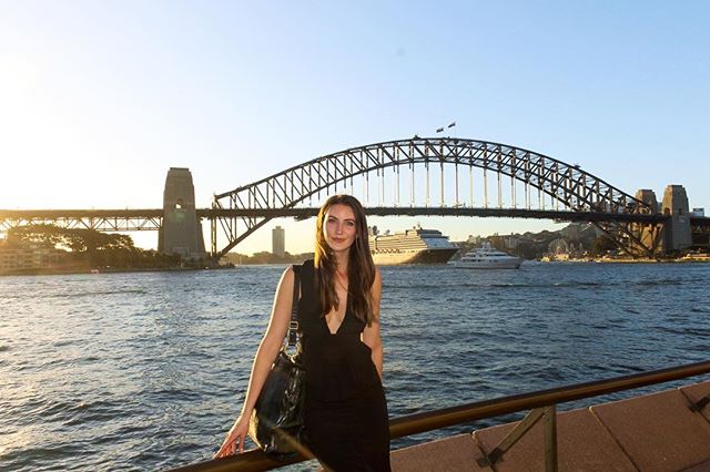 A woman in a dress poses near Sydney Harbour Bridge, enjoying the cityscape and calm waters.