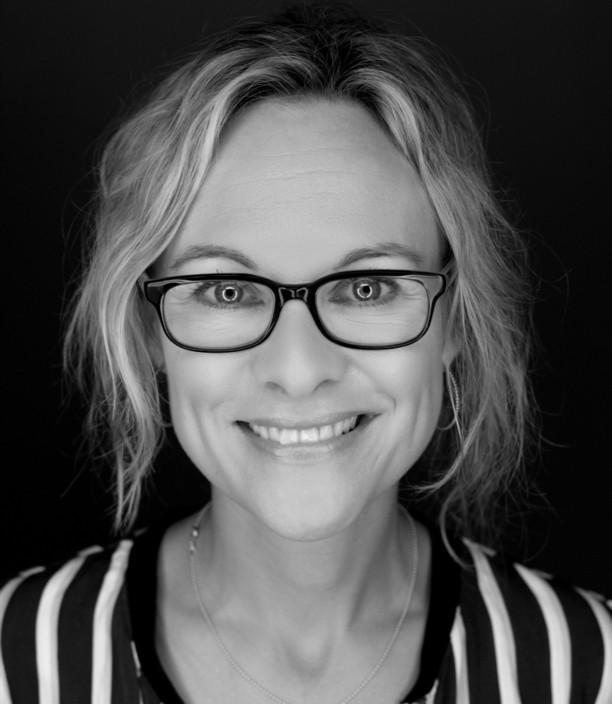 A smiling woman with glasses in black and white, perfect for a professional headshot or profile picture.